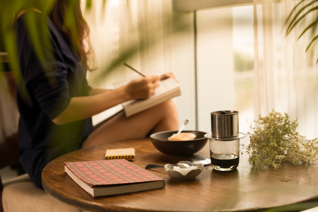 Femme écrivant dans un carnet, tasse de café et plantes vertes sur la table